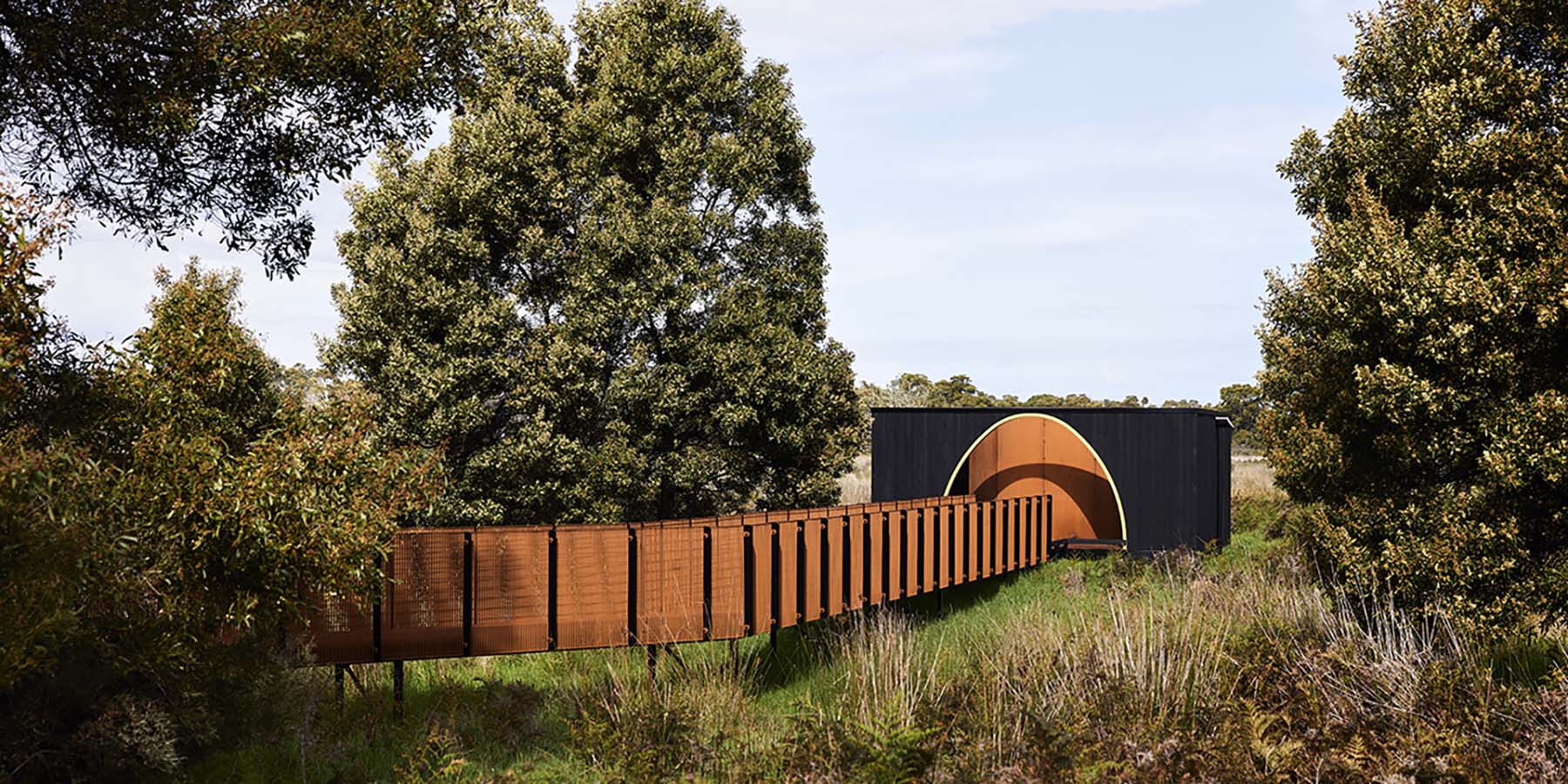 A weathered steel mesh walkway leads to a charred timber bird hide, set in a native bush landscape at Kurtontij IPA.