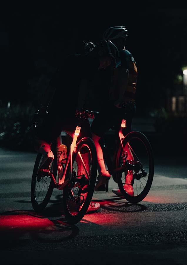 Two cyclists stopped on a bike path at night with Flock Lights shining light onto their legs.