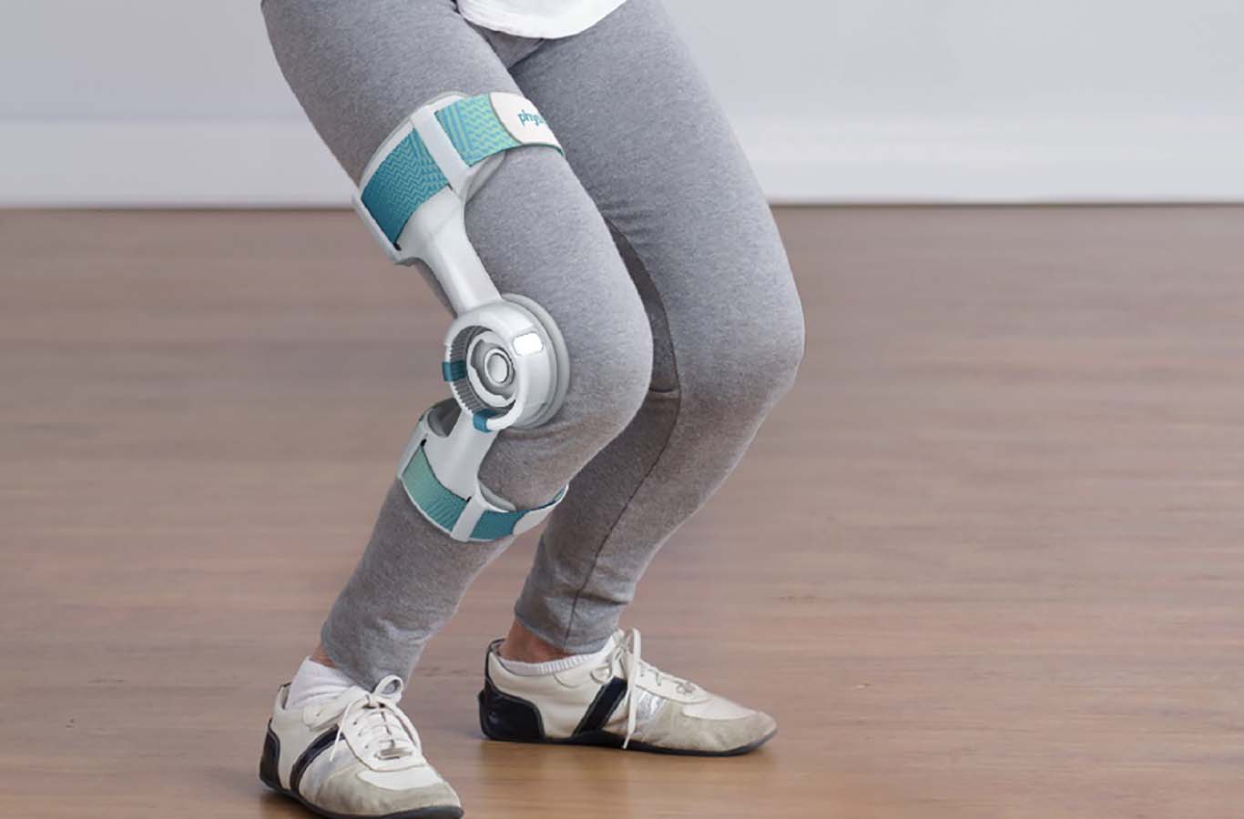 a pair of legs in grey tights and sneakers in a mini-squat, teal and grey brace worn on the right knee