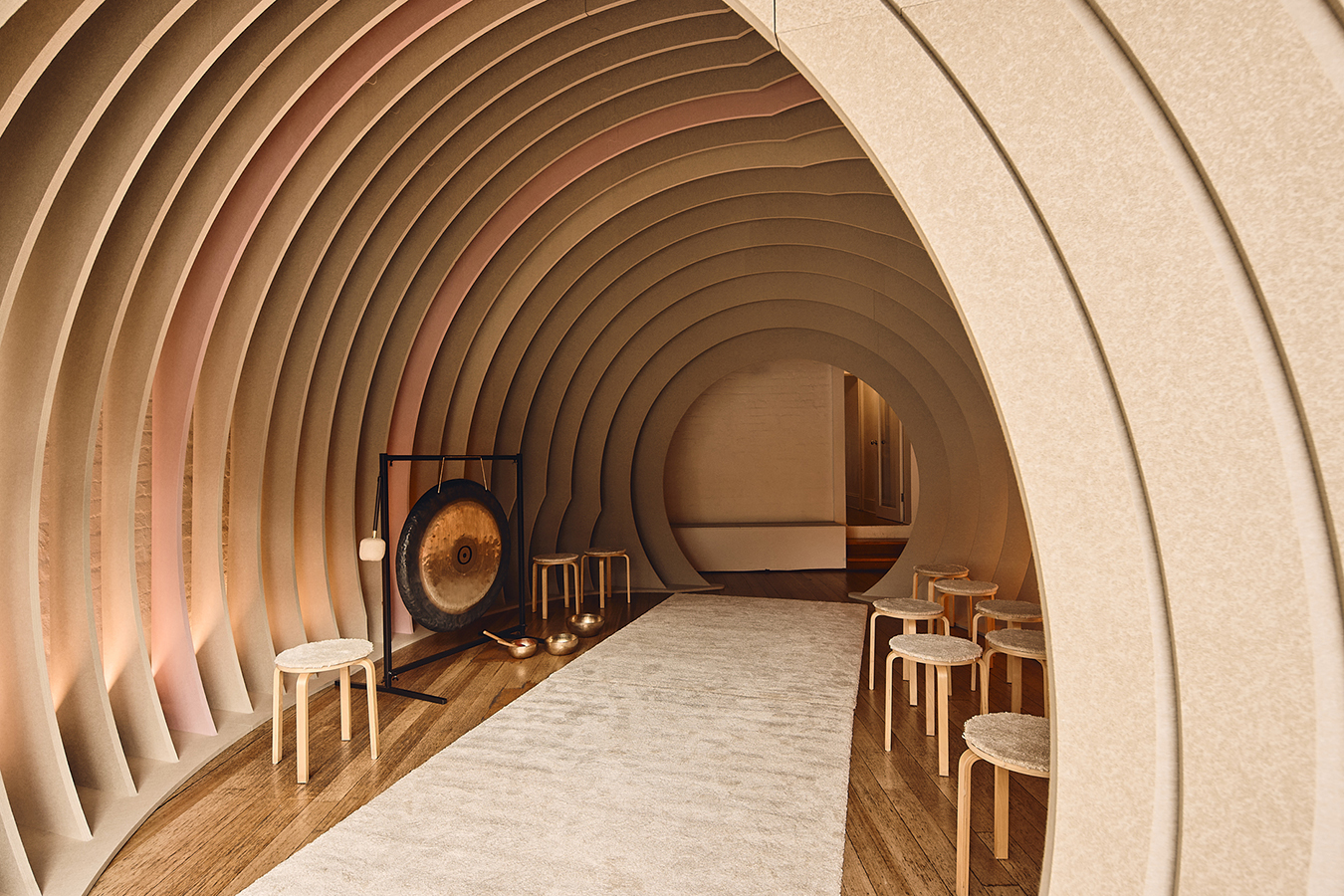 Interior view of curved room with gong and stools, warmly lit.