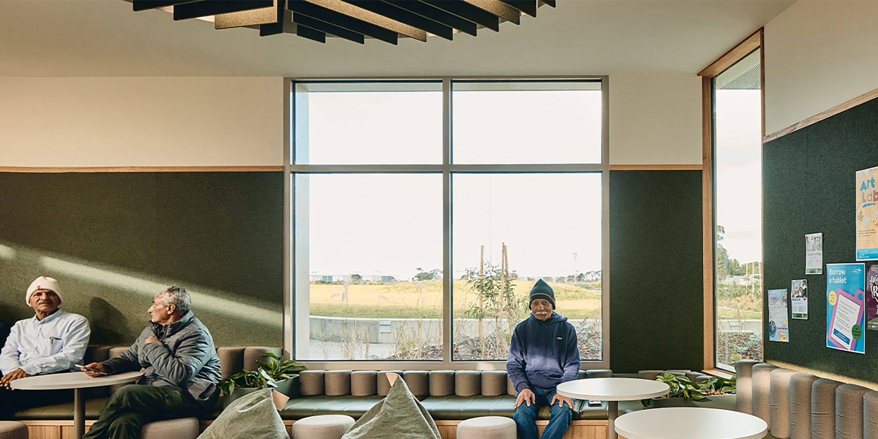 Three older men seated within the green youth library lounge.