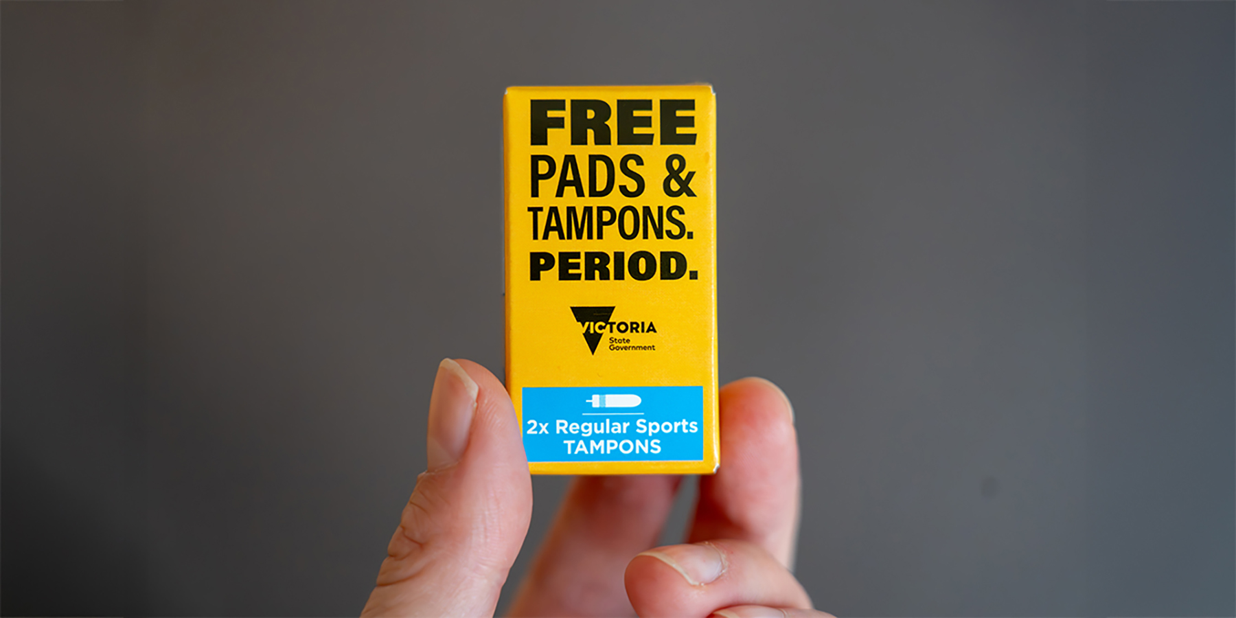 Close-up of a hand holding an orange tampon box featuring the campaign’s bold, minimal design.