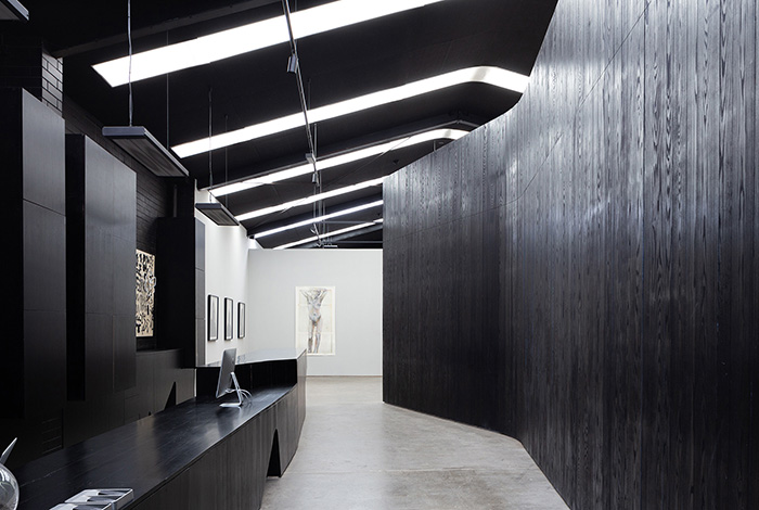 Entering into the gallery, only a glimpse of the art that lies beyond is given. Blackened timber walls guide visitors through
