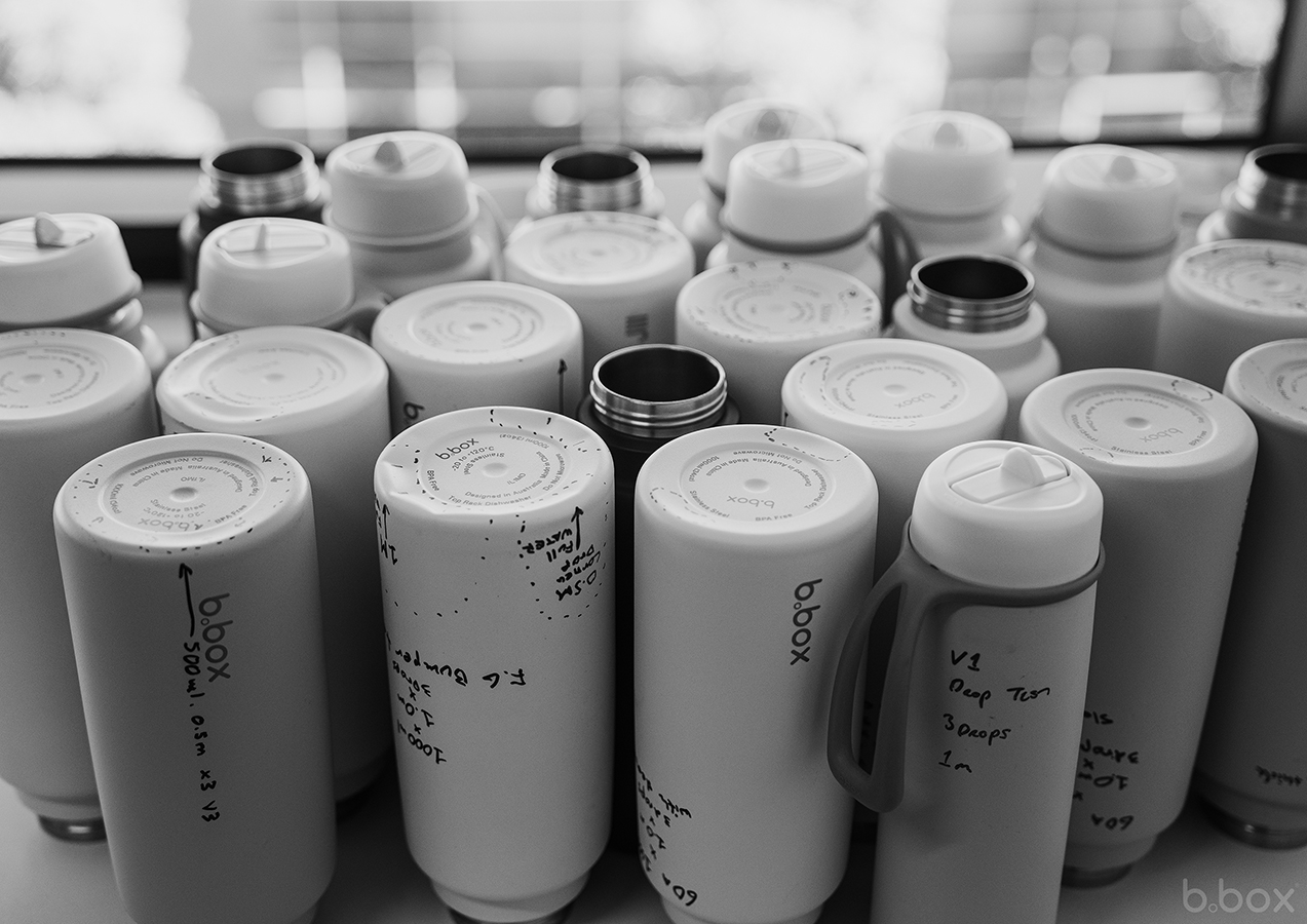 Close-up of multiple b.box bottles with test notes and drop test results, showcasing product durability and testing process.
