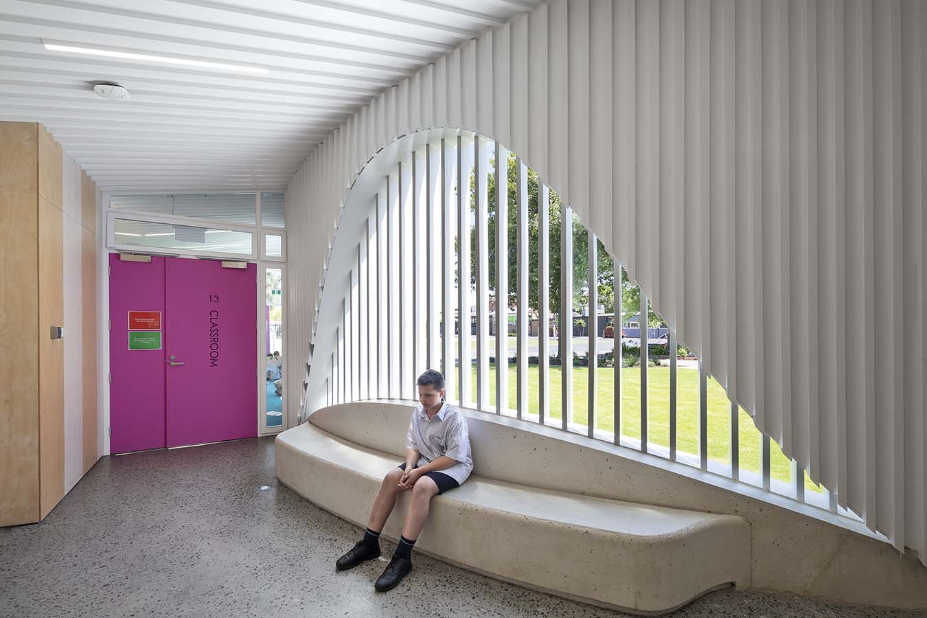 A student sitting on a bench seat inside the covered outdoor verandah of the PEGS Music Centre, an arched view to outside. Photo by John Gollings