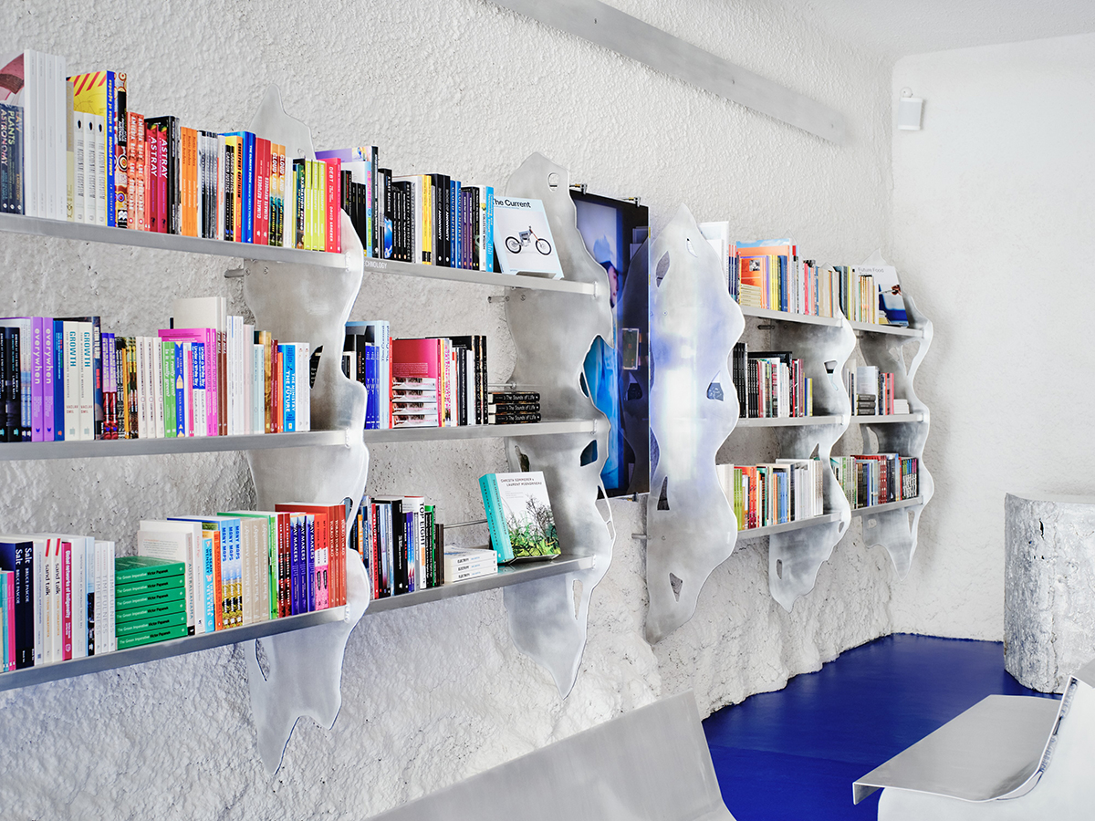 Contemporary bookshop interior with blue floor, aluminium benches, bookshelves, and vertical server screen.