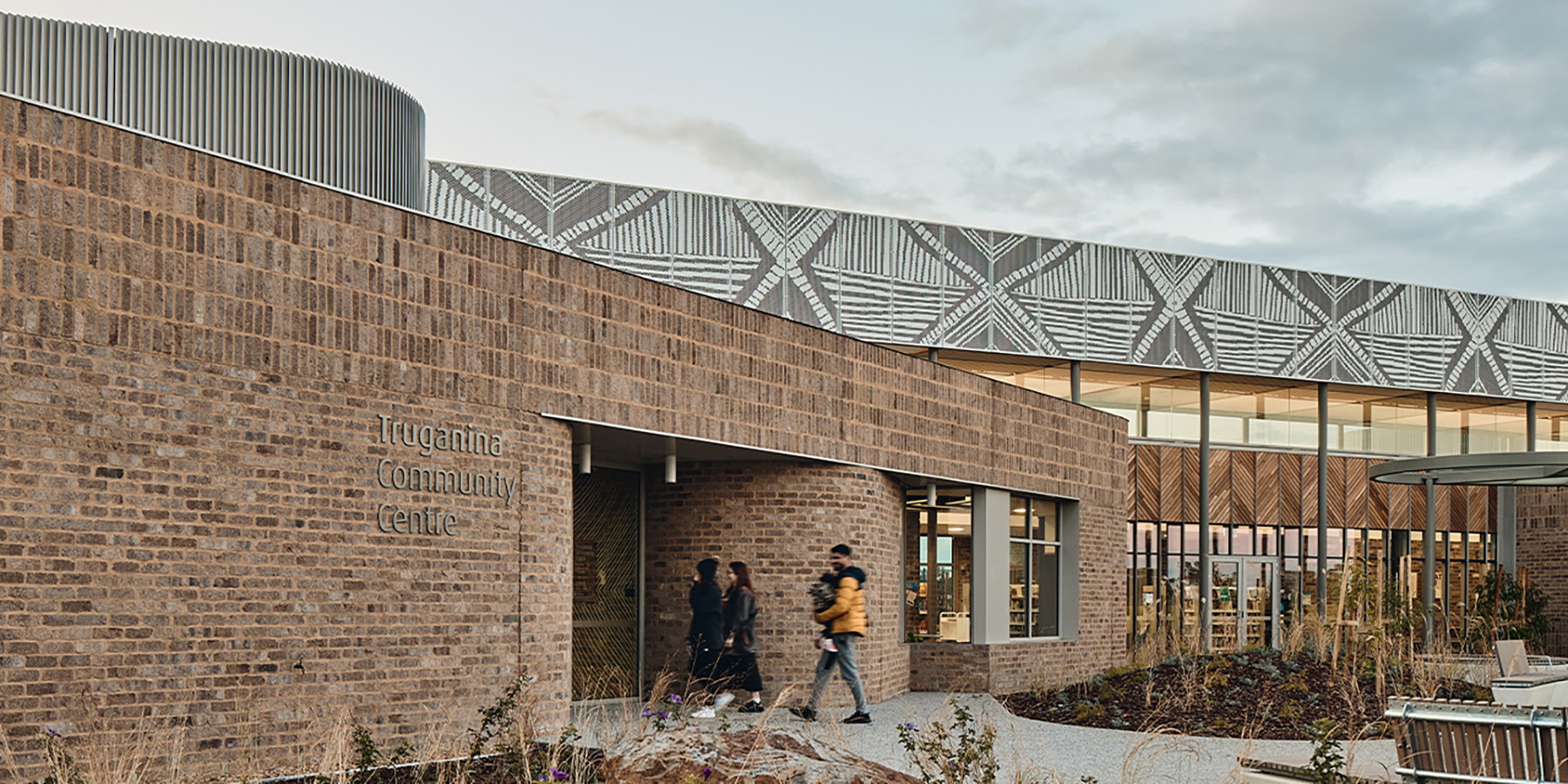 People entering the main entrance of the Truganina Community Centre. Artwork by Lisa Waup sits above the building.