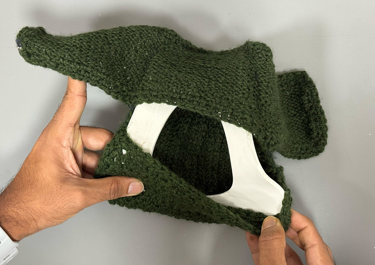 Hands holding a green knitted fabric wrapped around a white 3D-printed collar structure.