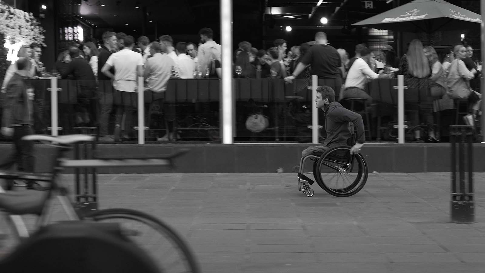 Image of a young male, pushing a Rove Wheelchair past a Melbourne bar.