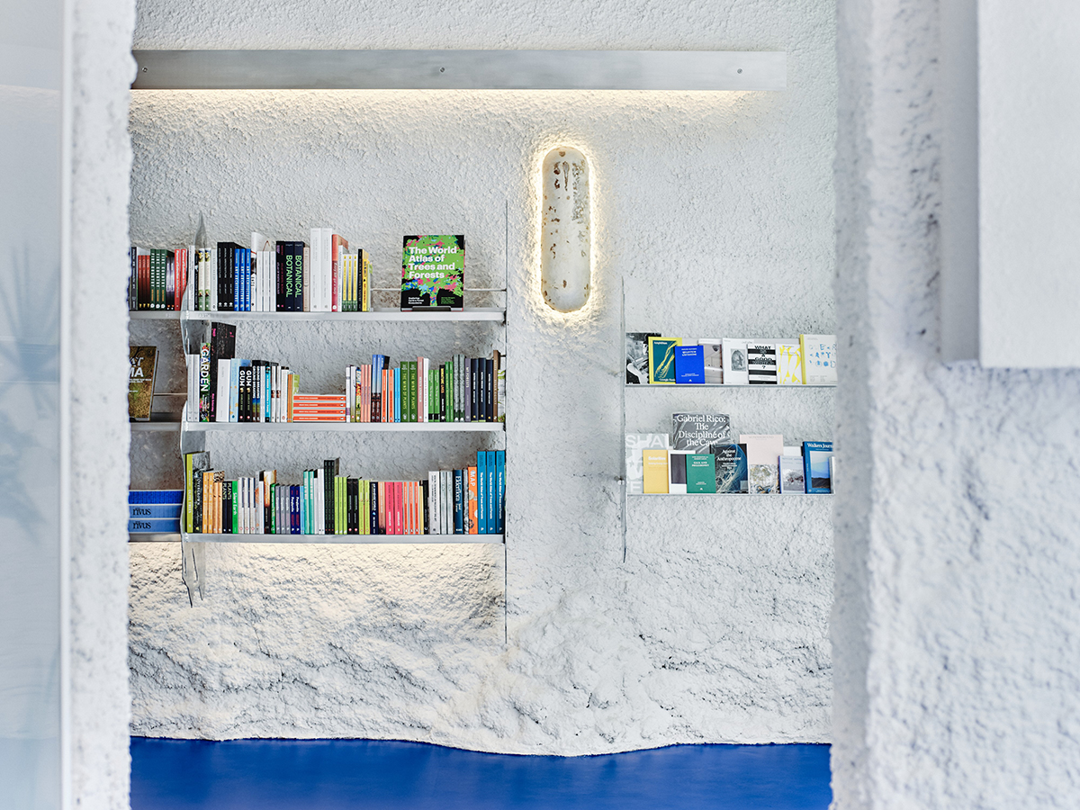 Contemporary bookshop interior with blue floor, aluminium bookshelves and featuring mycelium wall sconce.