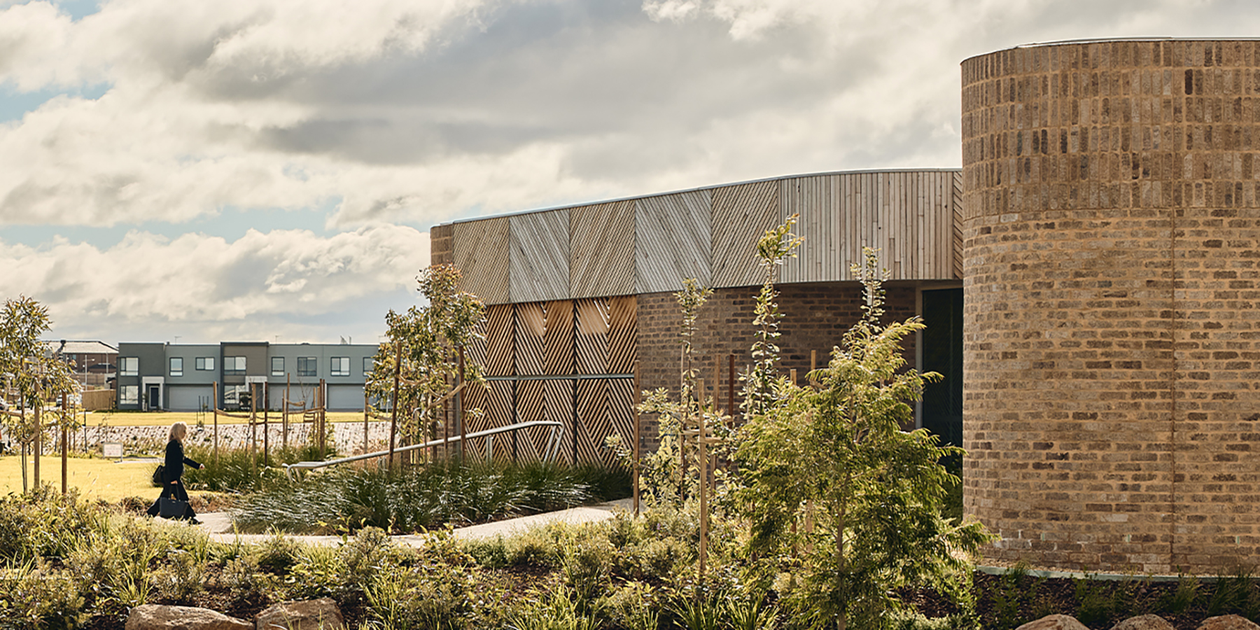 A person walking up through the ramped entrance of the building with landscaping surrounding on either side.