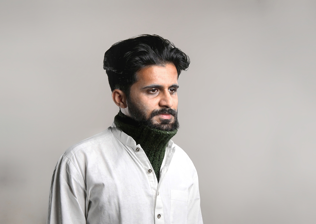 A man wearing a green knitted neck support collar over a white shirt, designed for discreet assistive device.