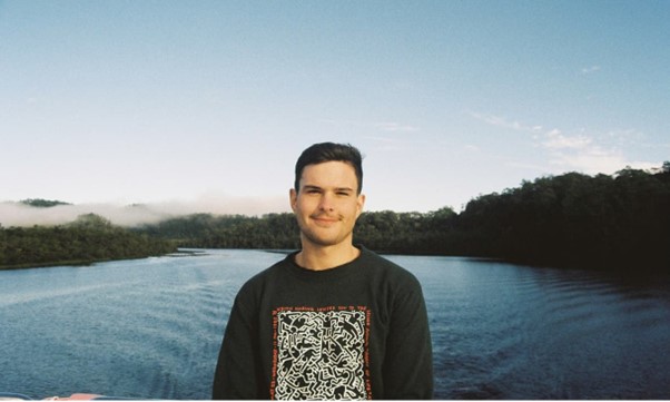 man in black jumper staring at camera standing in front of a lake