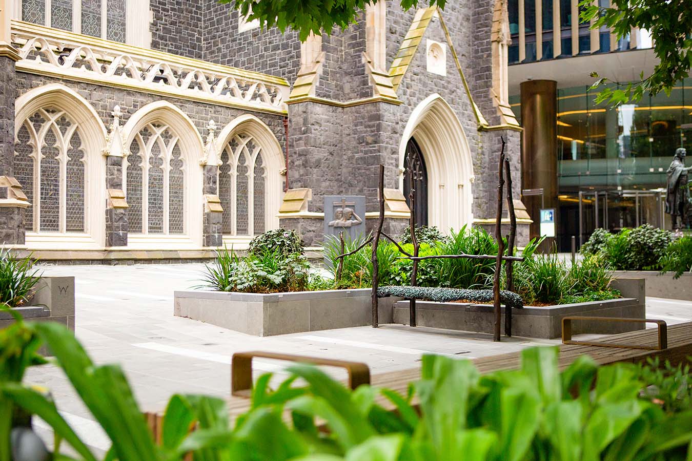 A photograph loooking through greenery to a variety of seating spaces in front of a historic bluestone church building.