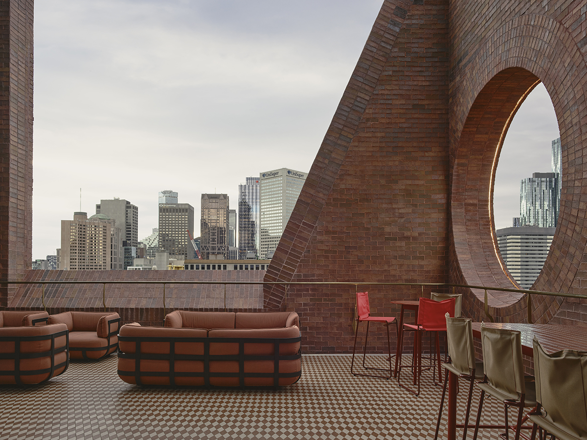 A roof top bar terrace with couches and red brick walls, circular cutouts frame views of Melbourne cityscape.