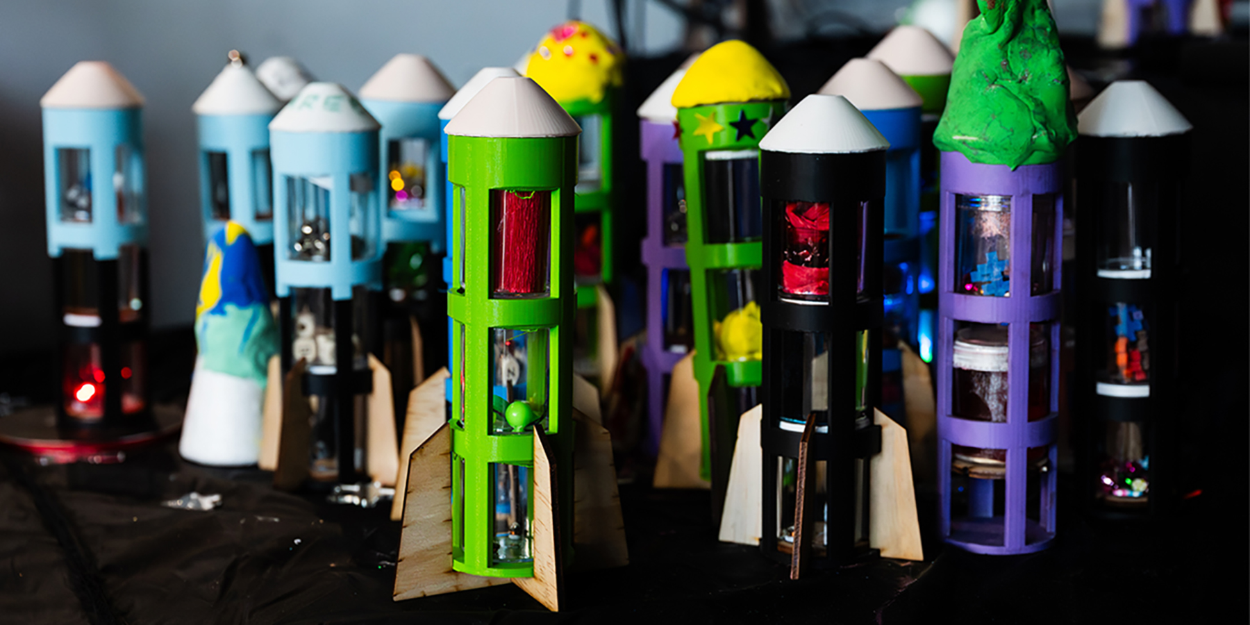 Decorated 3D-printed rockets stand upright, each uniquely styled with colours, textures, and lights.