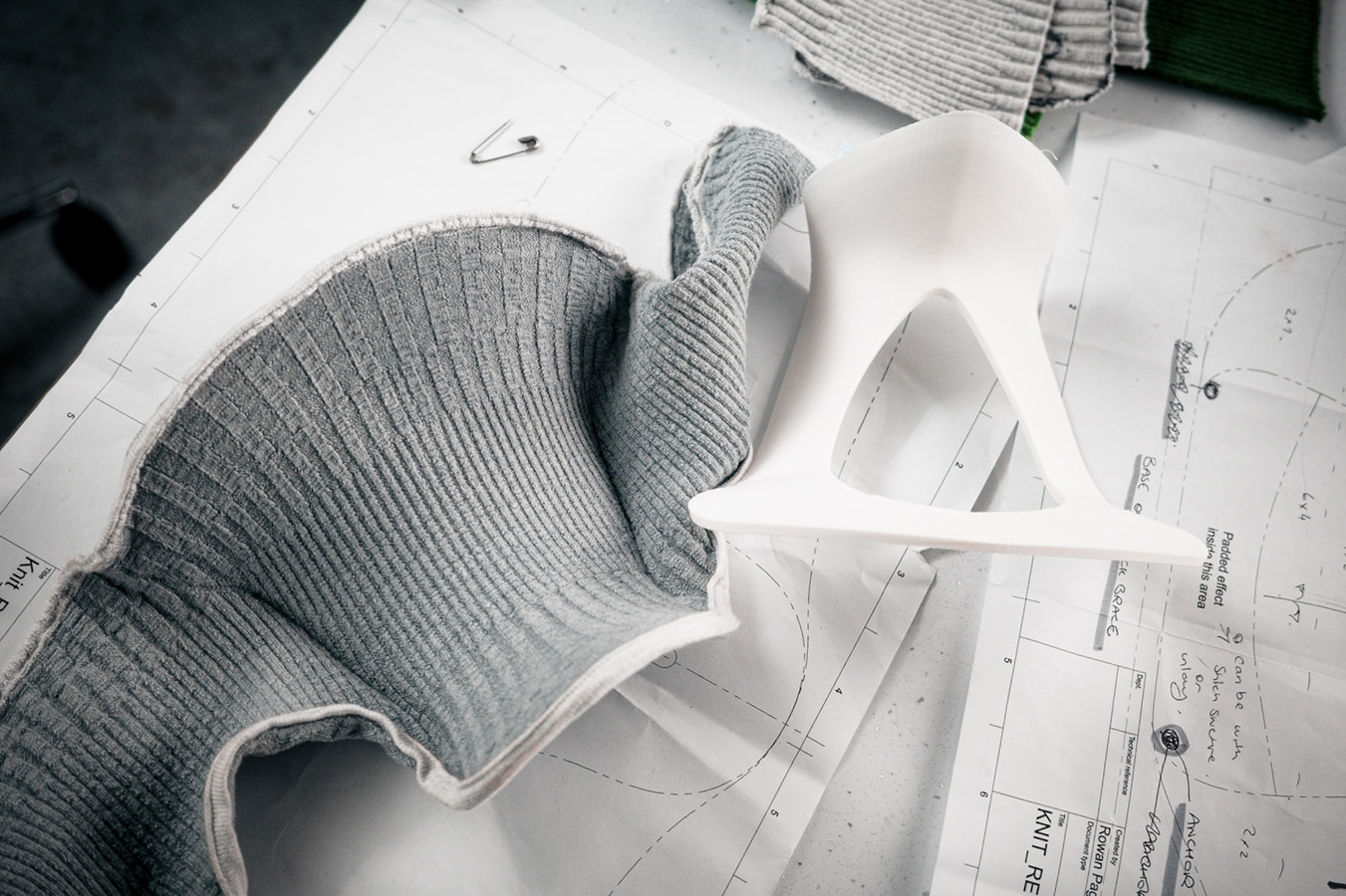 Gray ribbed fabric and a white 3D-printed collar frame placed on top of sewing patterns and design notes