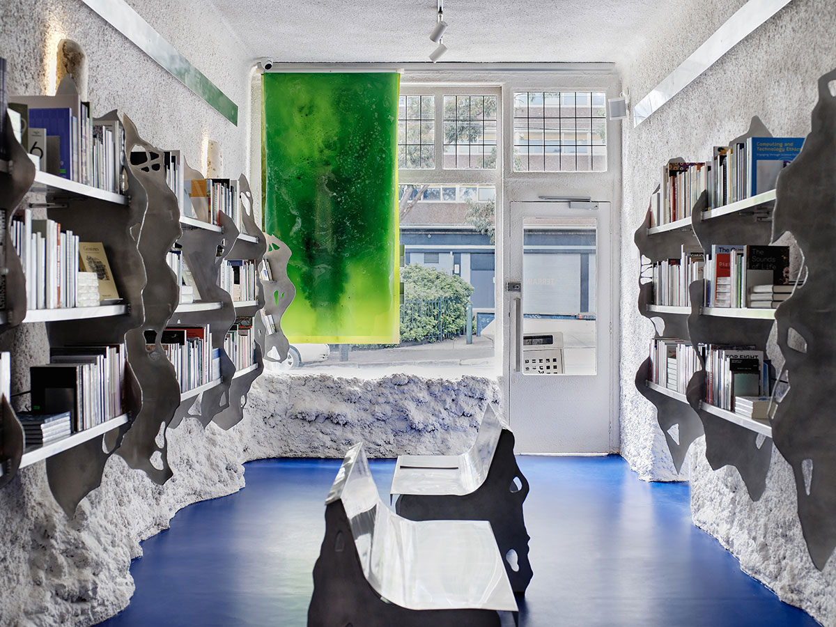 Contemporary bookshop interior with blue floor, algae-based bioplastic panel blinds, aluminium benches and bookshelves.