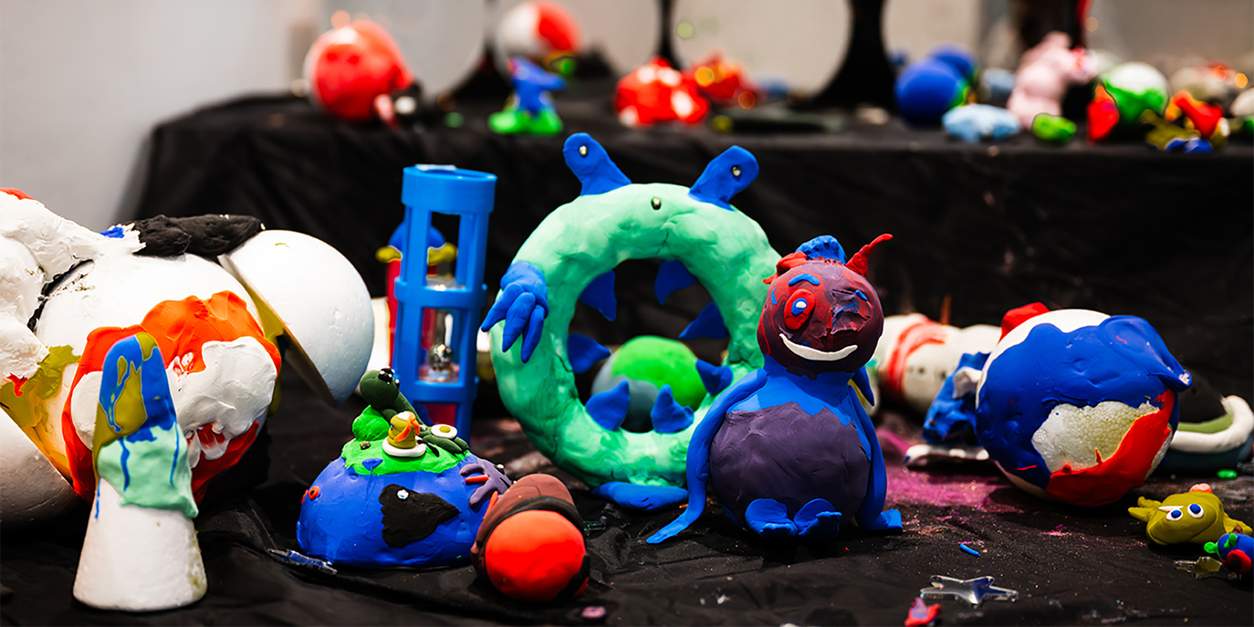 Bright handmade aliens and planets sit on a black cloth, inviting children to touch and explore.