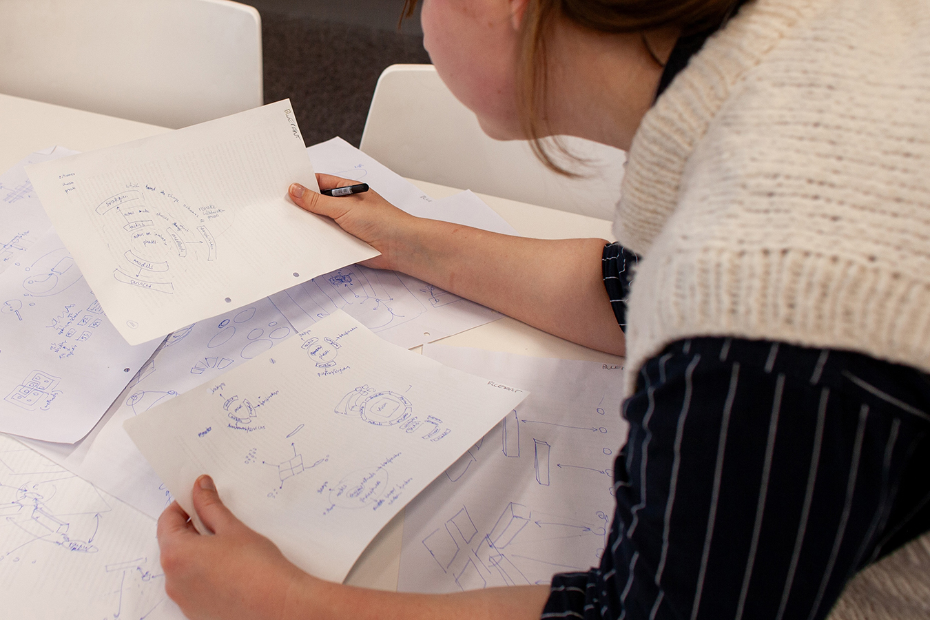 A person is leaning over drawings from the design process of the blueprint, she is holding two different pages.