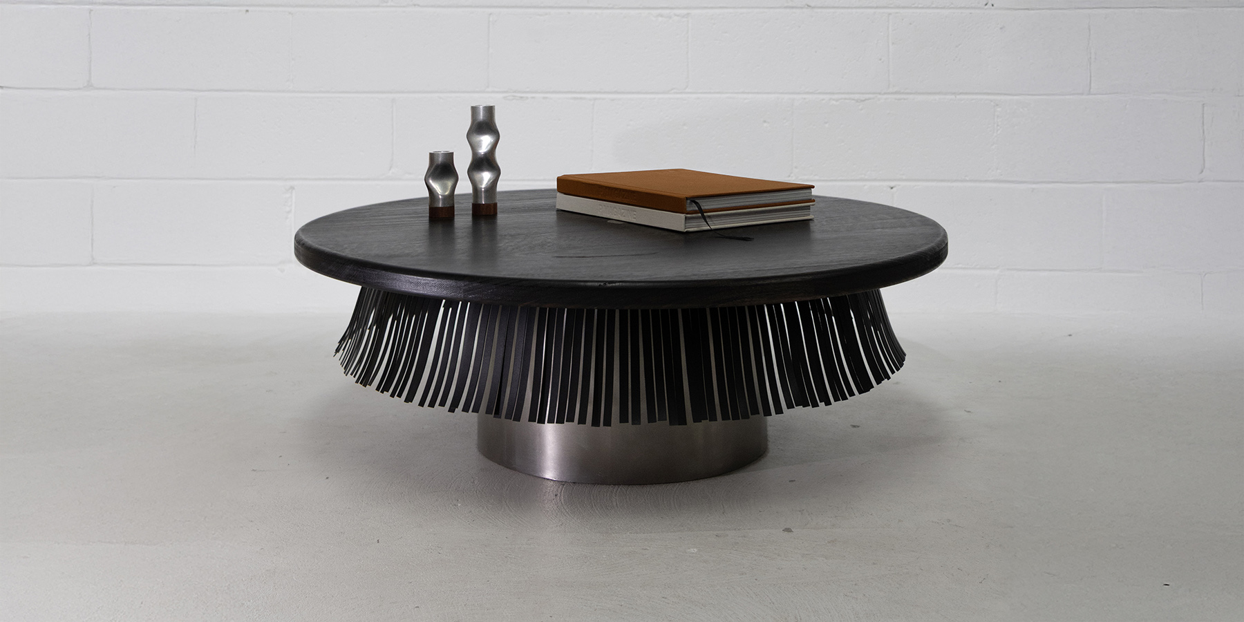 Orville Table by Locki Humphrey; a low, round coffee table with a steel cylinder base, timber top & hanging leather fringe.