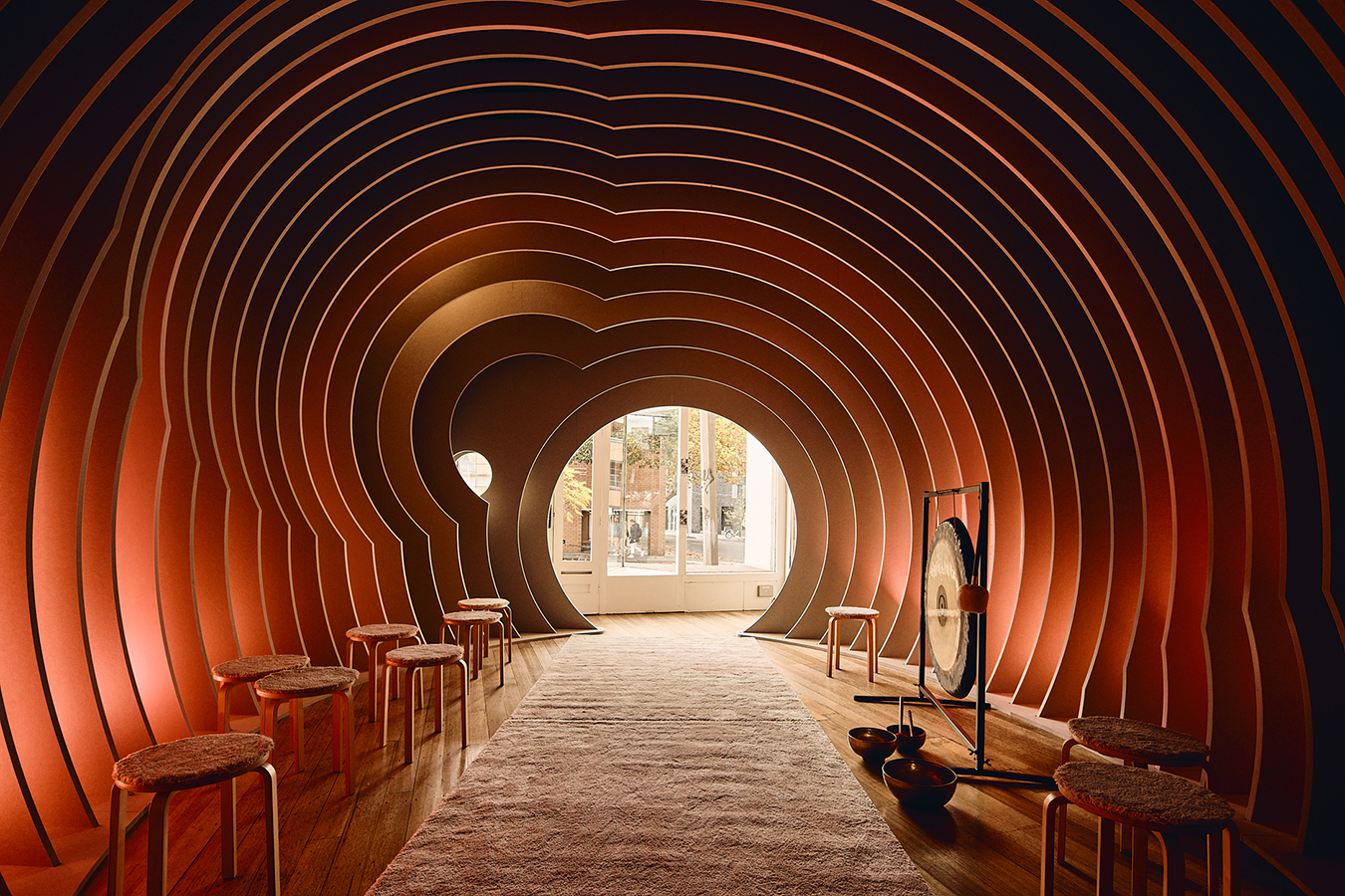 Empty curved room with stools lined up and a gong at one side.