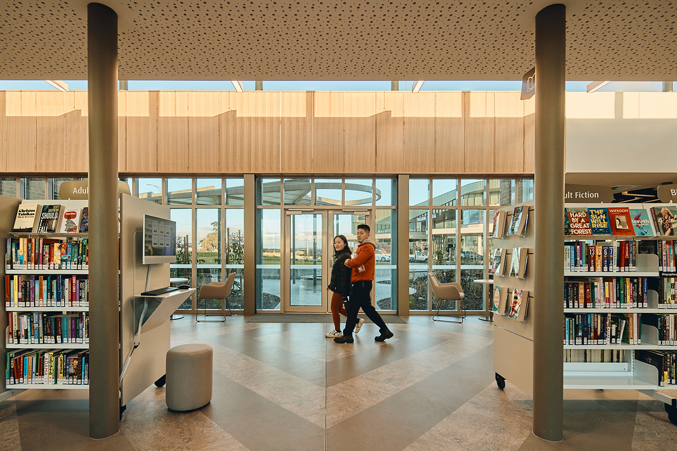 Two people walking across the main circulation space with shelving and natural light filtering in.