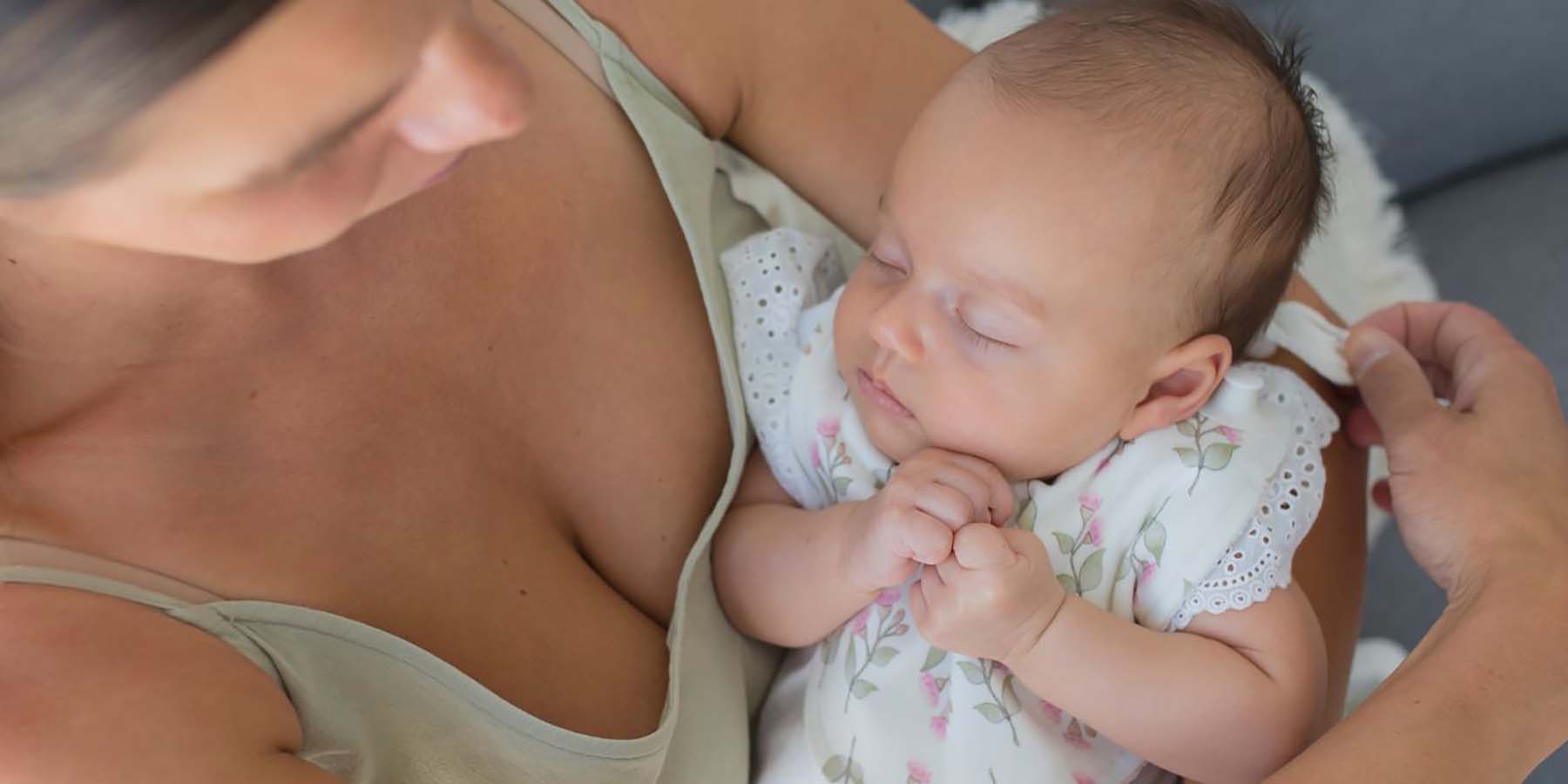 A mother holding her sleeping baby and removing her Gigi Bib with one hand.