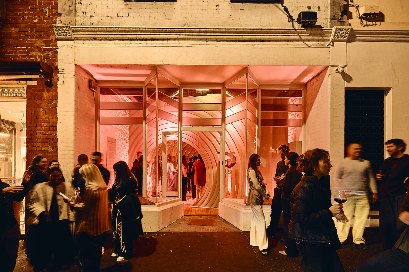 At night with glowing pink interior and people gathered outside.