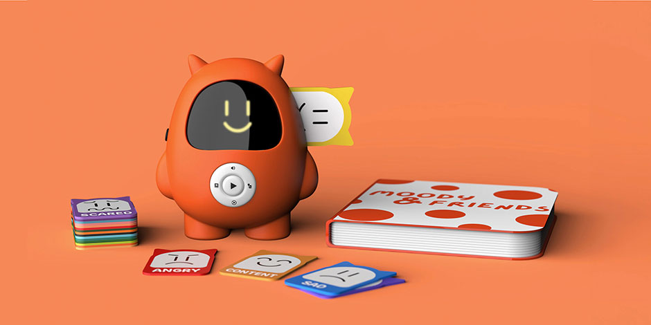 Moody, an orange toy, displays a smiling face with a happy emotion card inserted, beside emotion cards and a storybook.