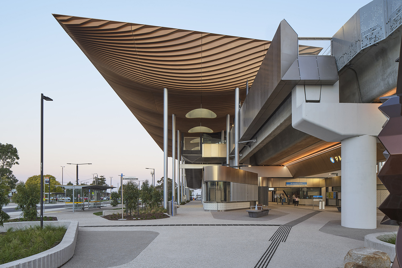Entry plaza at Pakenham Station with soaring timber roof, sculptural columns, seating, and landscaped forecourt.