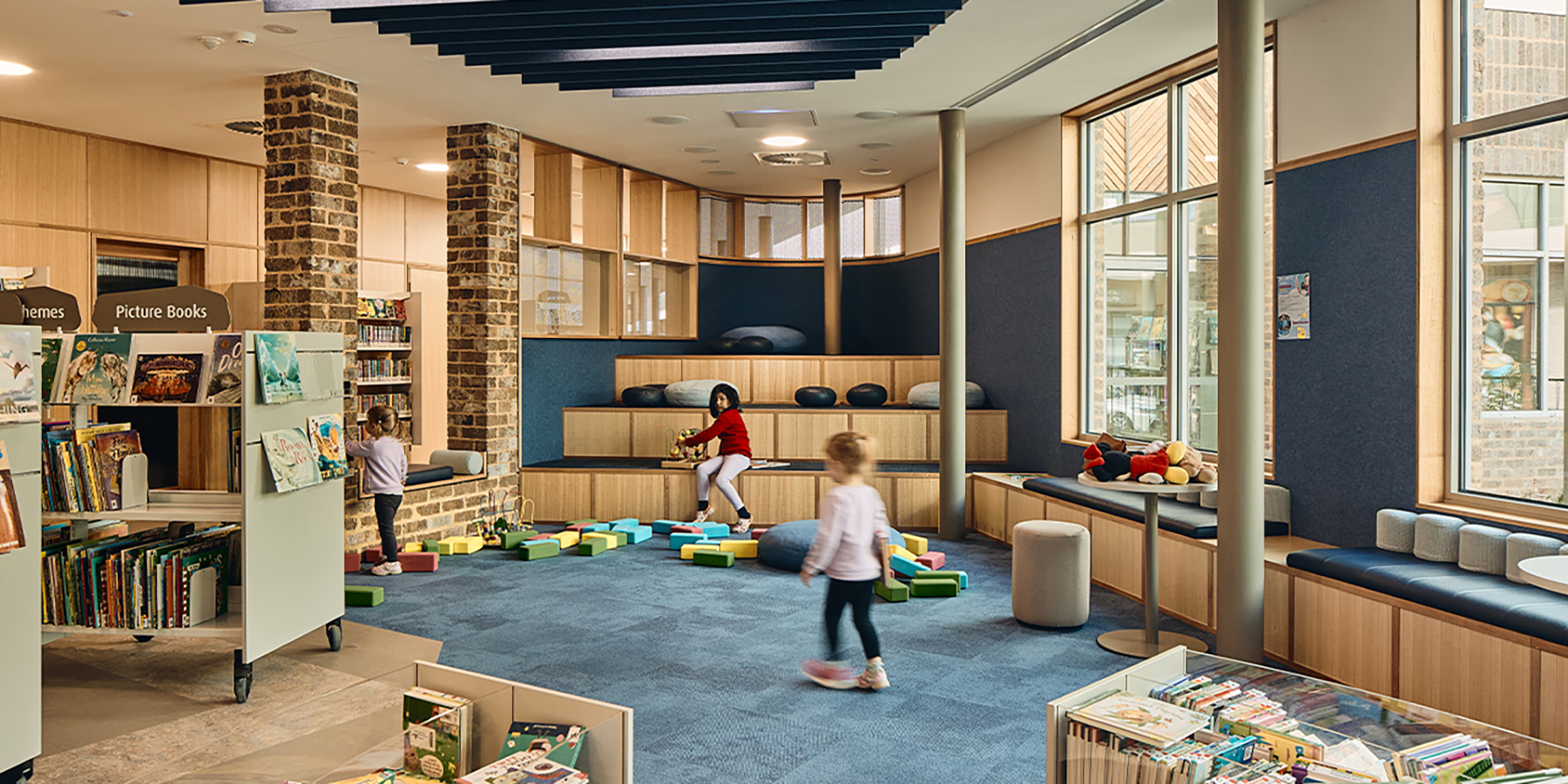 Children playing in the blue children's library lounge amongst toys and shelving.