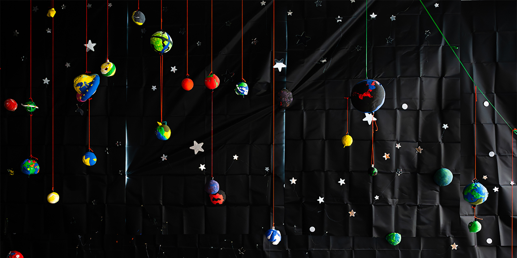 Planets hang on red strings against a starry black backdrop, creating a floating galaxy wall.