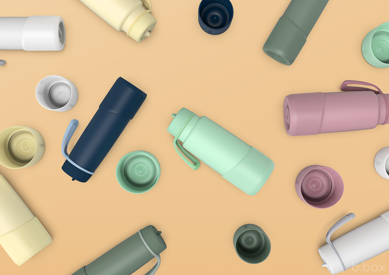Colourful b.box insulated drink bottles with matching bumpers scattered on warm beige background, shown from top-down view.
