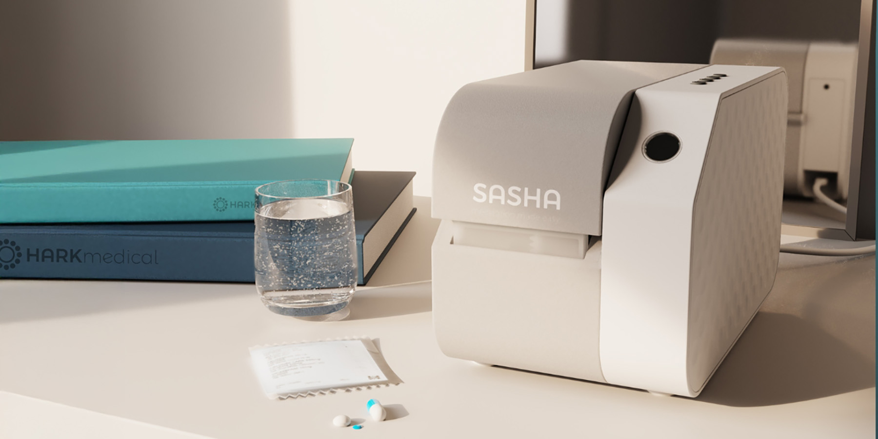 A close up of a connected medication management device on a table with books, water, a medication sachet, and pills.