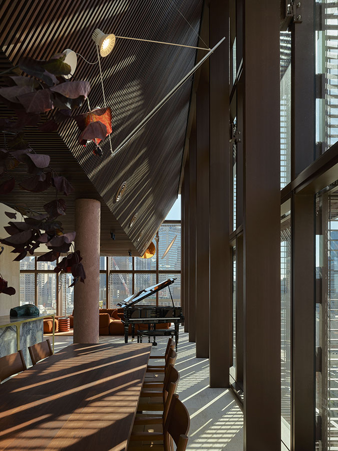 A spacious room with double height ceiling, featuring a piano and large windows allowing natural light to fill the space.