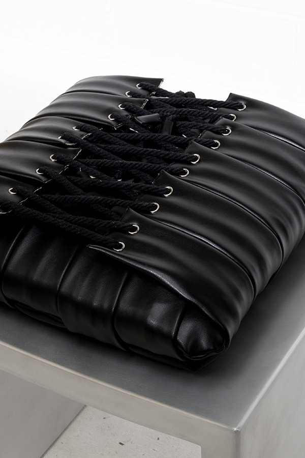 Underside of the woven Vault Stool cushion, revealing a corset closure using black cotton cord and steel eyelets.